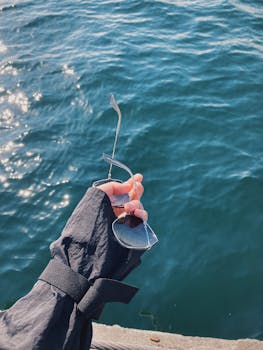 A close-up of a hand holding sunglasses over the sparkling blue waters of Istanbul.