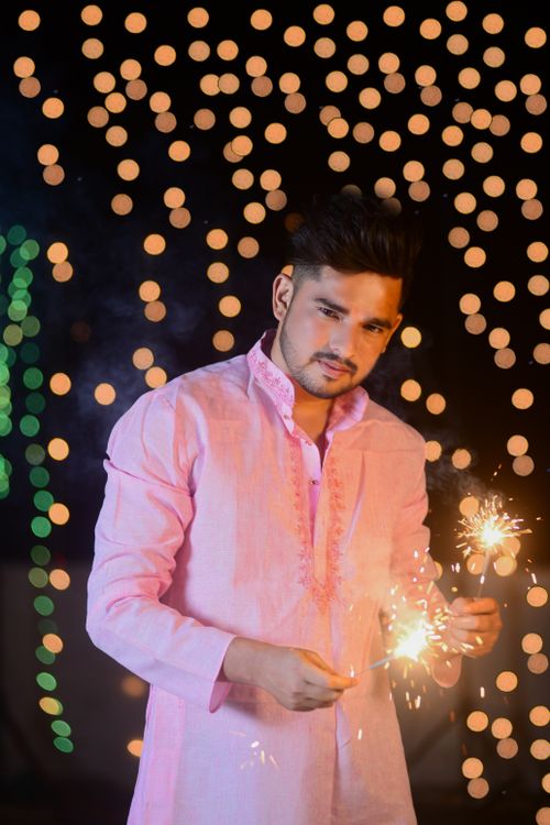 Free Young man in pink attire holding sparklers, celebrating during nighttime festivities with bokeh lights in the background. Stock Photo