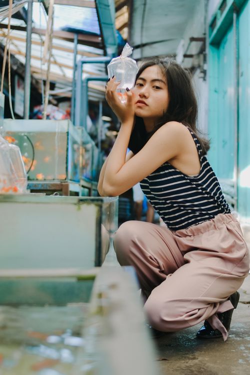 Free Asian woman crouched indoors, holding a bag with fish in a vibrant Indonesian market. Stock Photo