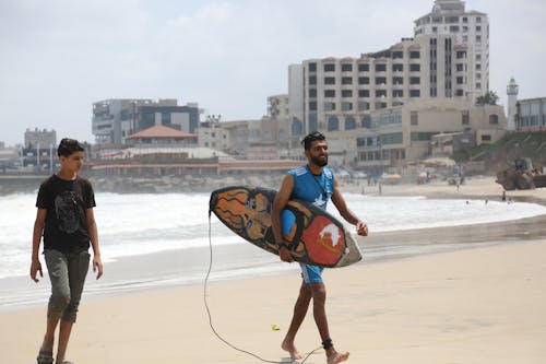 A Man with a Surfboard Walking Near a Boy