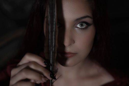 A dramatic portrait of a woman with striking eyes, holding a feather, creating a mysterious mood.