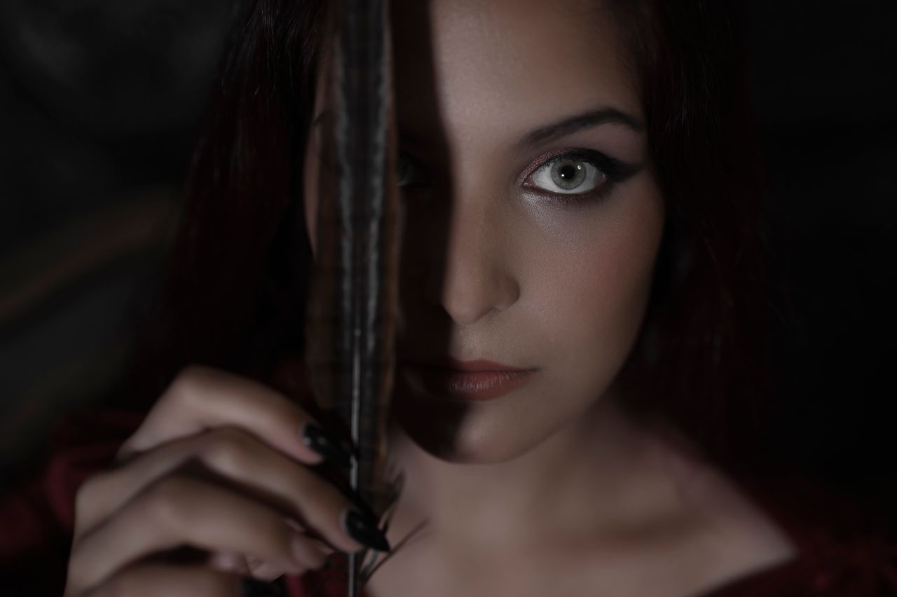 a dramatic portrait of a woman with striking eyes holding a feather cr