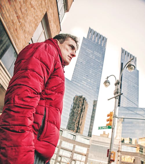 Man Wearing Red Bubble Coat Standing Under Tall Buildings