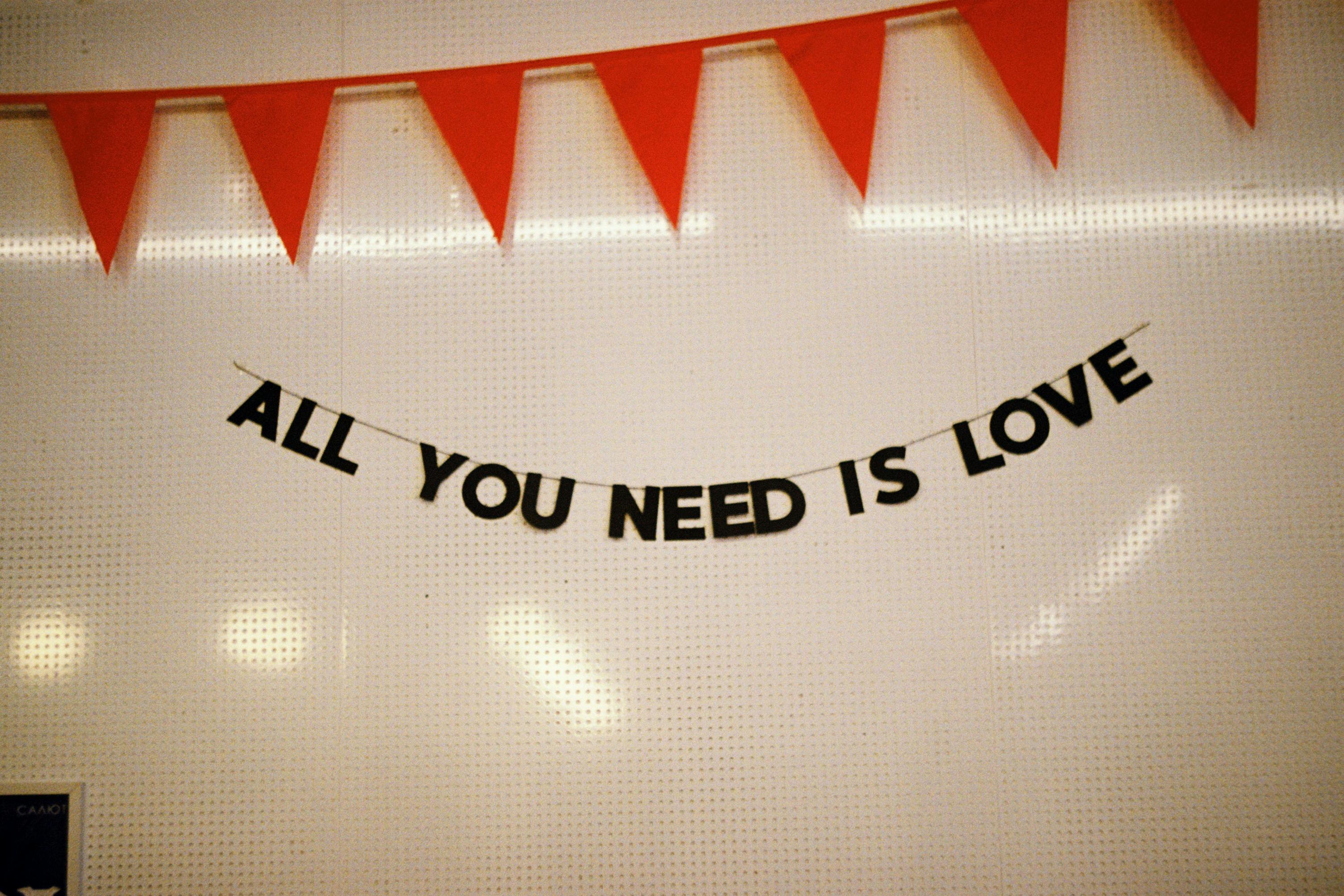 A string of letters spelling 'All You Need Is Love' with red bunting on a wall.