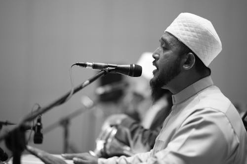 A Grayscale Photo of a Man Talking in Front of the Microphone