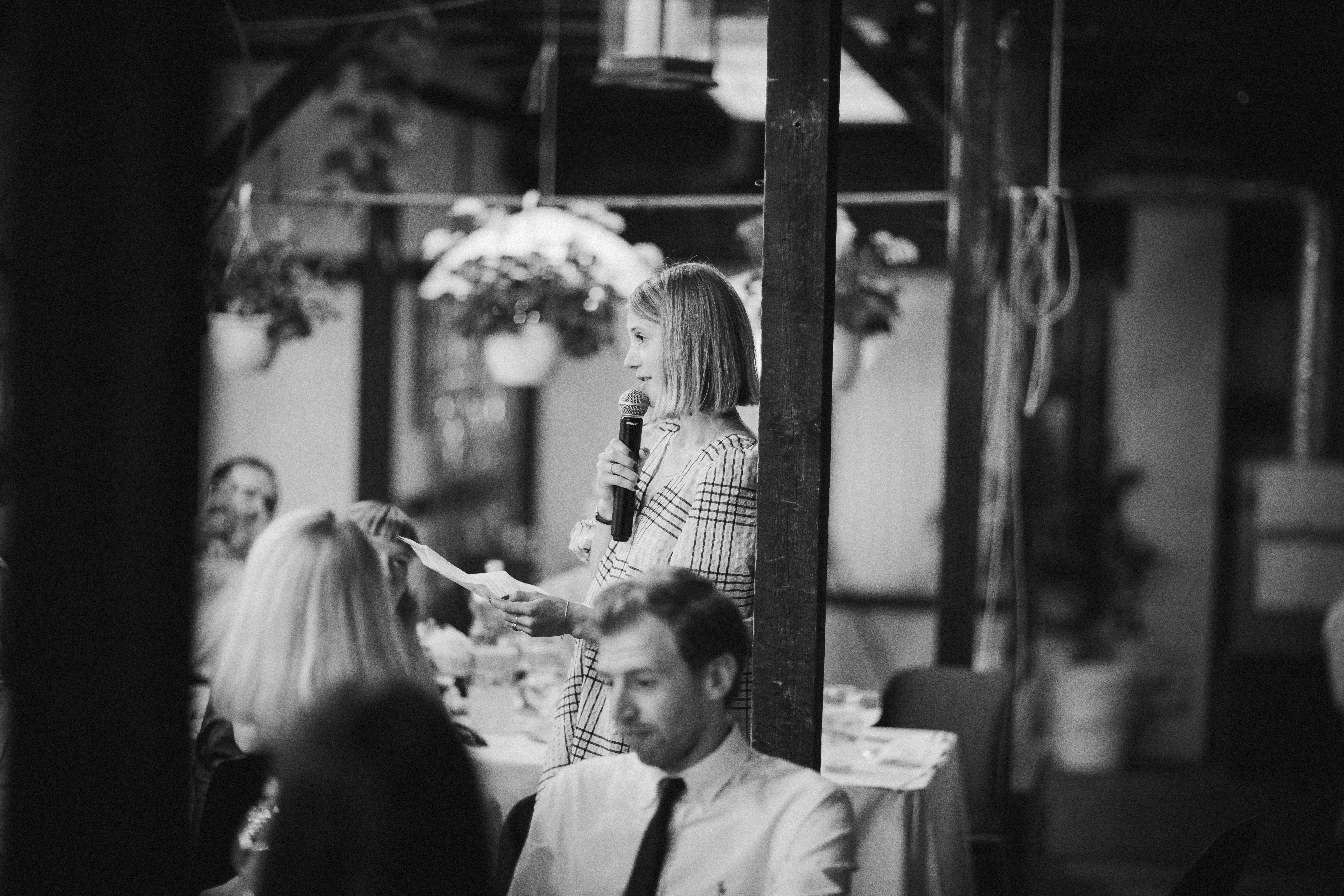 Une femme parle dans un microphone lors d'un rassemblement intérieur, symbolisant le rôle d'un animateur photobooth pour engager les invités et gérer le flux.