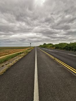 Discover the serene expanse of an empty road under a dramatic, cloudy sky in Merseyside, UK.