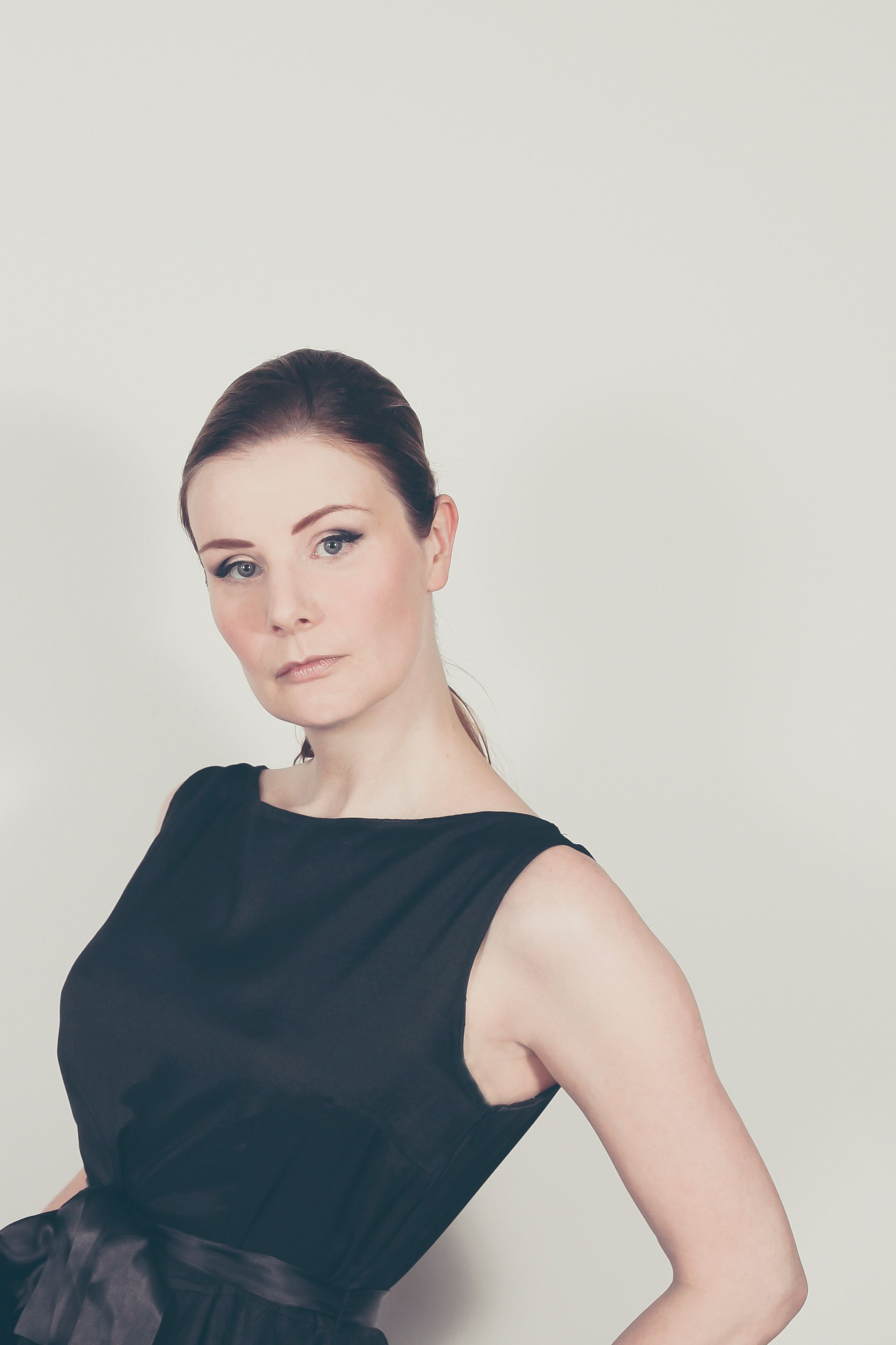 Studio portrait of a woman in classic black dress showcasing elegance and poise.