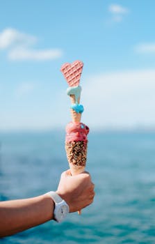 Triple-scoop ice cream cone with heart-shaped wafer held against the ocean.