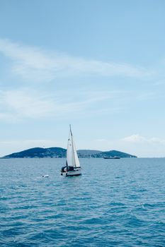 A serene scene of a sailboat navigating the open ocean with islands in the distance.
