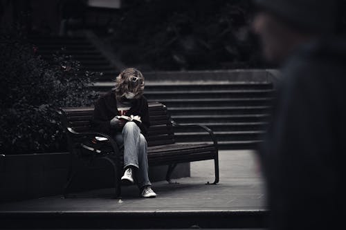 Free Woman Reading Book While Sitting on a Bench Stock Photo