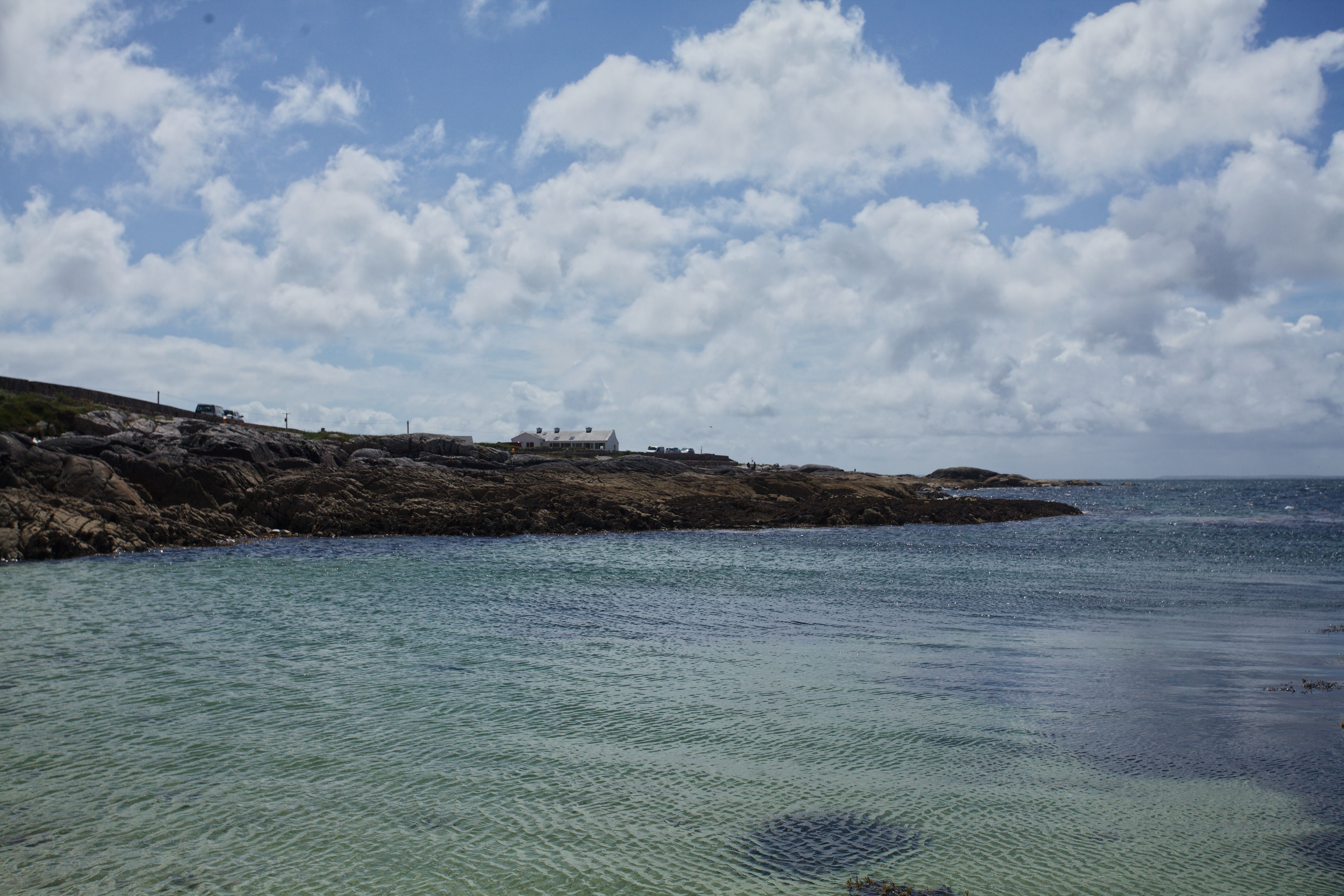 Beautiful rocky coastline in Ireland with clear water and cloudy sky.
