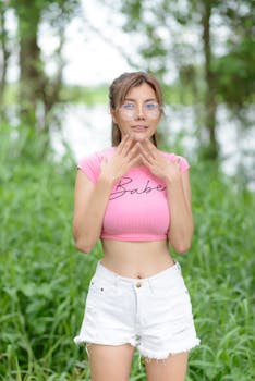 Smiling woman in pink top posing outdoors, with a blurred nature background.