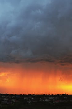A stunning scene of rain beneath a dramatic sunset sky, showcasing nature's beauty over a small town.