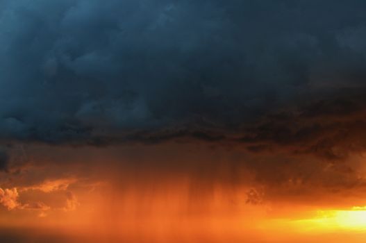 Vivid storm clouds with rain illuminated by a striking sunset sky.