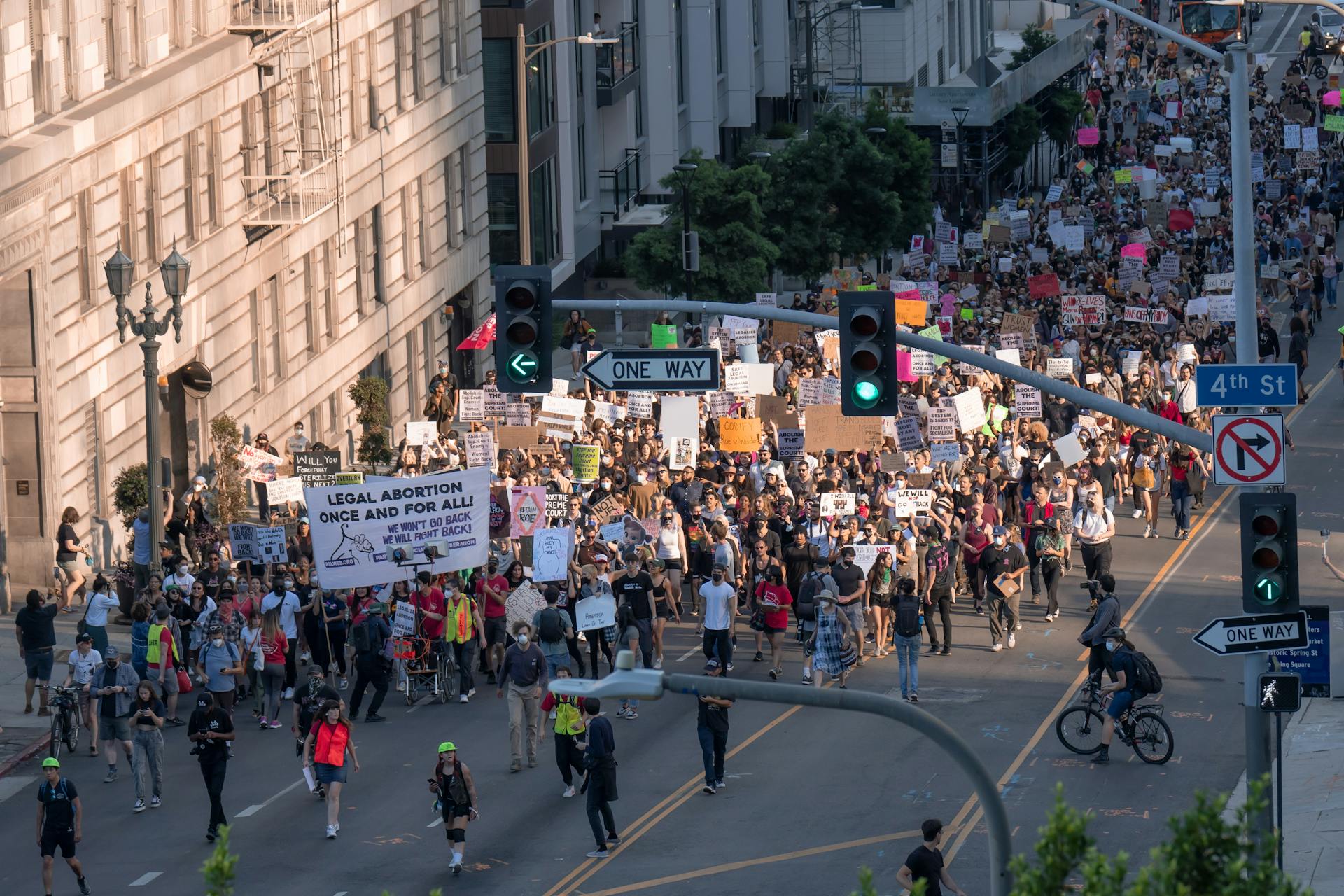 A diverse crowd in Los Angeles rallies for legal abortion rights, holding various placards on a city street.