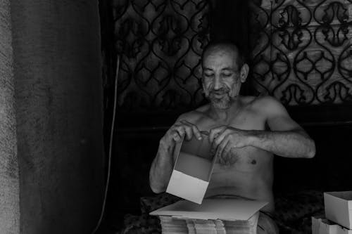 Grayscale Photo of a Topless Elderly Man Holding a Box