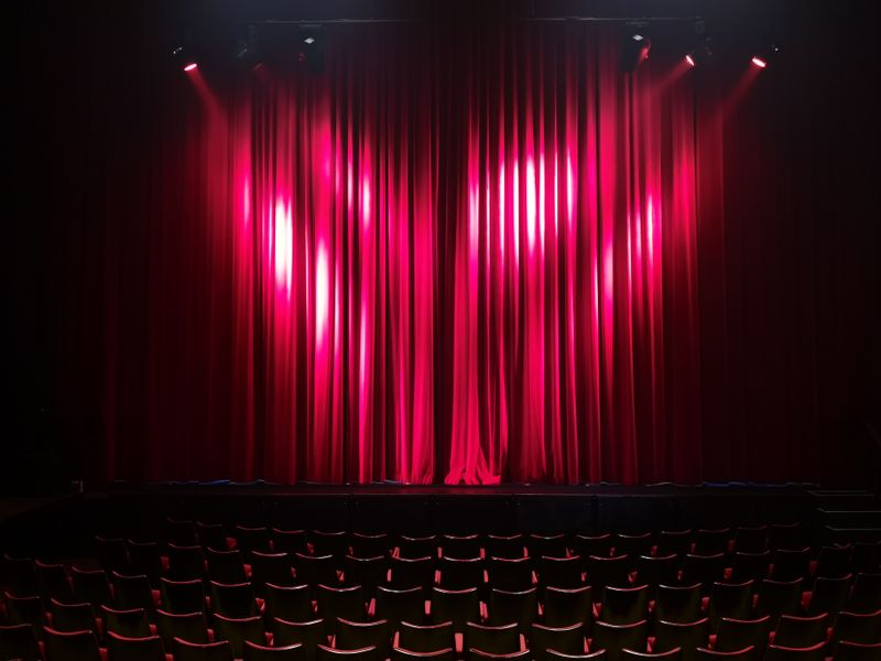 Lit red stage curtain above empty seats — photo by Ann H on Pexels