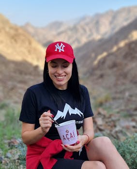 Smiling woman in red cap enjoying an açai bowl outdoors in the scenic Fujairah mountains.