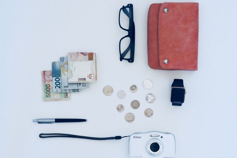 Flat lay of everyday items including currency, coins, wallet, and gadgets, all on a white background.
