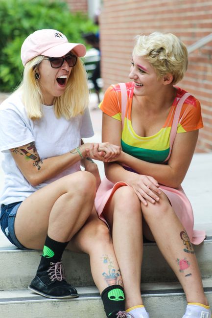 Two happy friends sitting outdoors, sharing a laugh while holding hands.