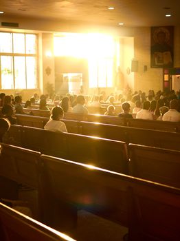 Sunlit church interior filled with people during a service, highlighting a serene religious atmosphere.
