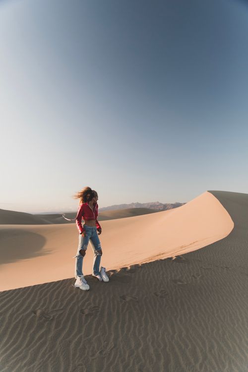 Free A woman stands on a sunlit sand dune in the desert, capturing a serene and adventurous moment. Stock Photo
