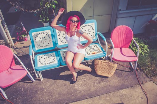 Stylish woman in a white dress and wide-brim hat posing on a sunny day with vibrant retro furniture.