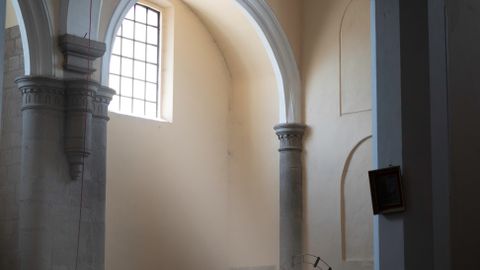 Calm church interior with sunlight streaming through arched windows onto empty pews.