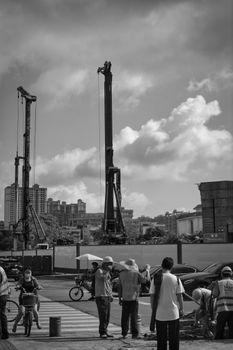 Black and white image of construction workers at a city site with cranes and pedestrians.