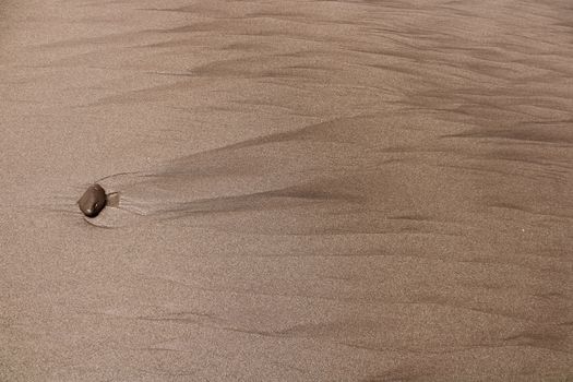Close-up view of textured sand with a single pebble creating a ripple effect.