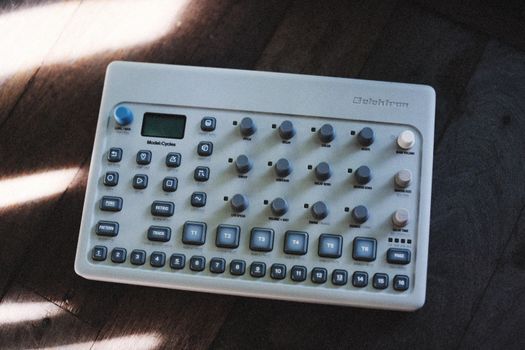 A top view of an Elektron Model:Cycles groovebox laid on a textured wooden floor.