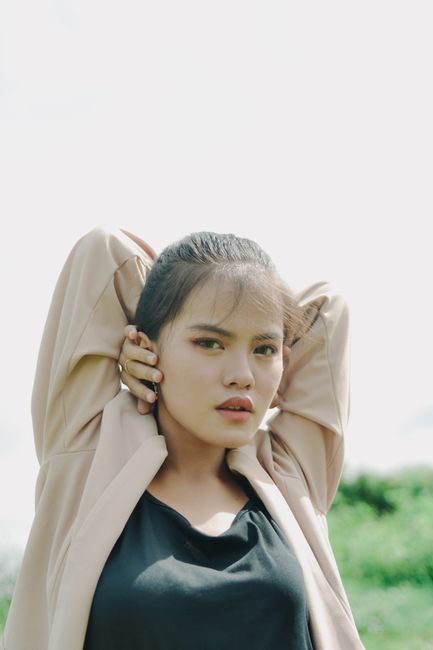 Natural light portrait of a woman posing with hands behind head outdoors in Indonesia.