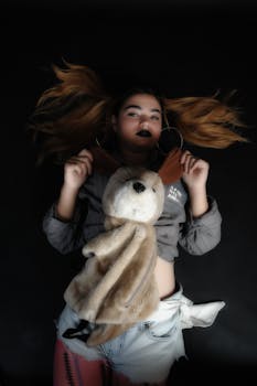 Stylish woman poses with toy on dark background, showcasing unique fashion style.