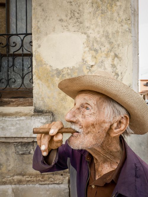 Free Portrait of a senior man in a hat smoking a cigar, captured outdoors. Stock Photo