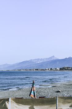 A serene beach scene with mountains in the background, showcasing an ocean umbrella on the sandy shore.