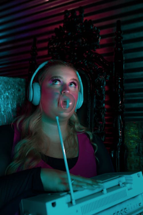 A Woman with Headphones Blowing a Bubble Gum