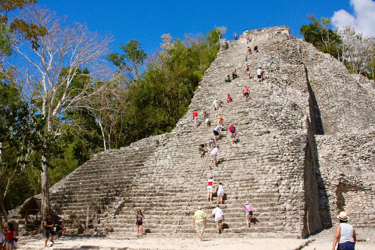 Los turistas exploran y escalan la antigua pirámide de piedra en medio de una exuberante selva
