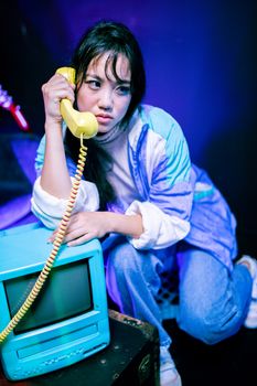Asian woman in retro attire with a vintage telephone and TV for a nostalgic vibe.