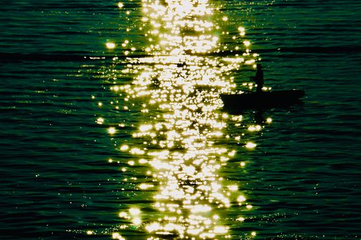 A silhouette of a person in a boat reflecting light on a tranquil body of water during sunset.