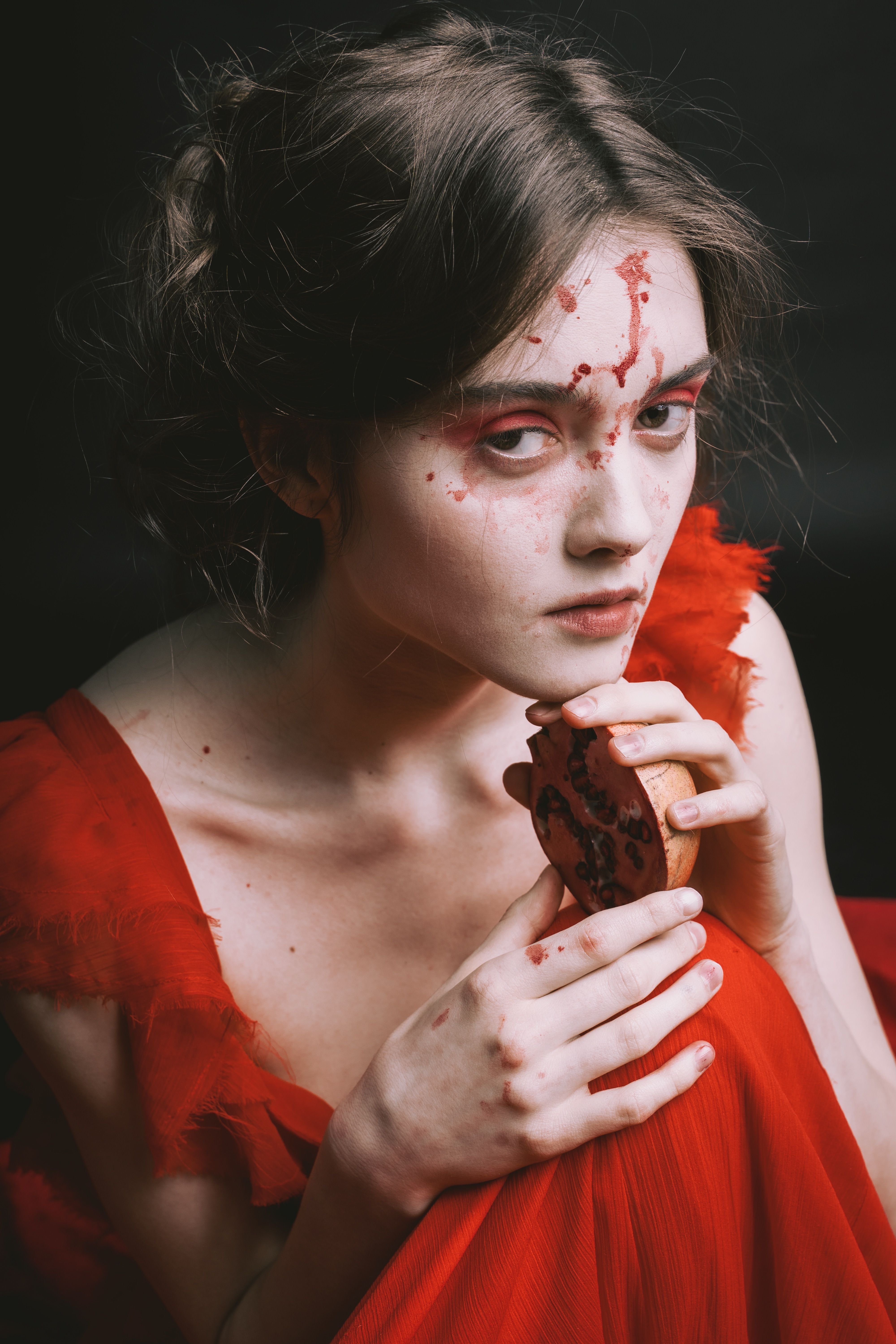 Artistic portrait of a woman in a red dress, holding a pomegranate, with creative makeup.