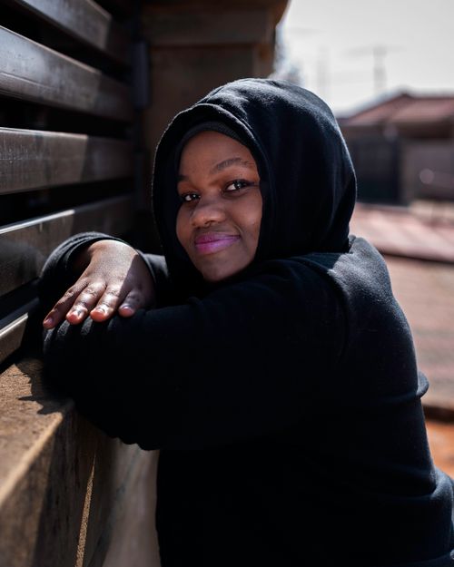 Free Portrait of a smiling woman in a black hoodie leaning against a wall outdoors. Stock Photo