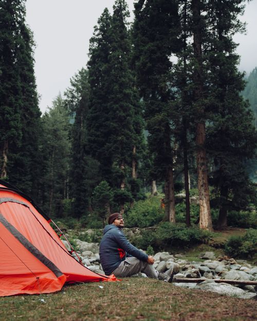 Free Adult male camper in forest setting sits by bright tent, enjoying nature. Calm and adventurous landscape. Stock Photo