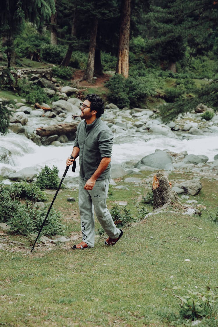 Man Holding Stick While Walking Beside River