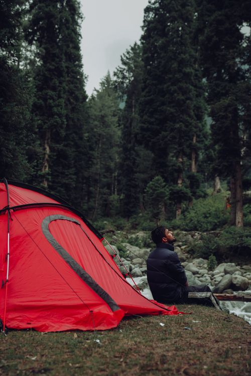 Free A man enjoys solitude by a red tent in a lush forest setting. Stock Photo