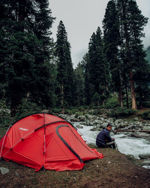 Photo of a Man Sitting near a Red Camping Tent