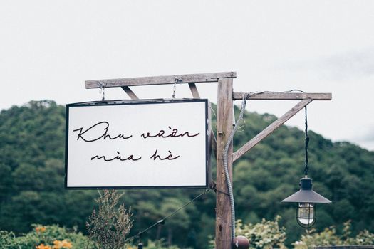 Elegant sign against a lush forest background with hanging lamp, creating a serene outdoor ambiance.