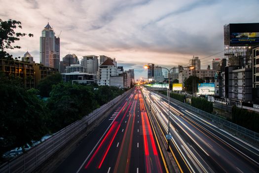Vivid cityscape featuring a bustling highway with light trails at twilight, showcasing urban life and architecture.