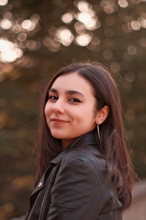 Free Smiling woman with long hair and hoop earrings posing outdoors in a black leather jacket. Stock Photo