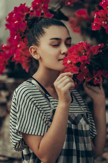 Young woman smelling vibrant red bougainvillea flowers with eyes closed, expressing tranquility and